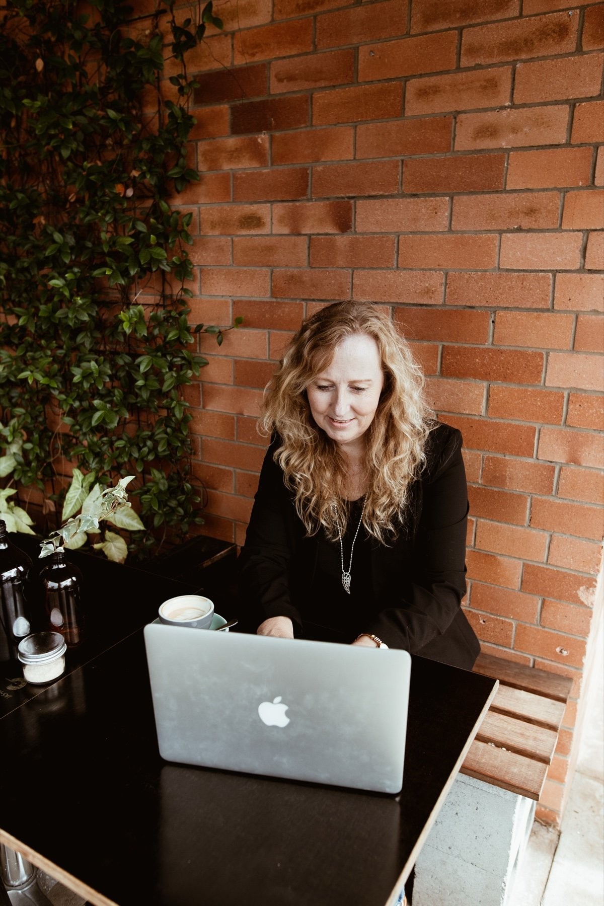 Lyn Baird writing at a café table with her laptop and coffee.