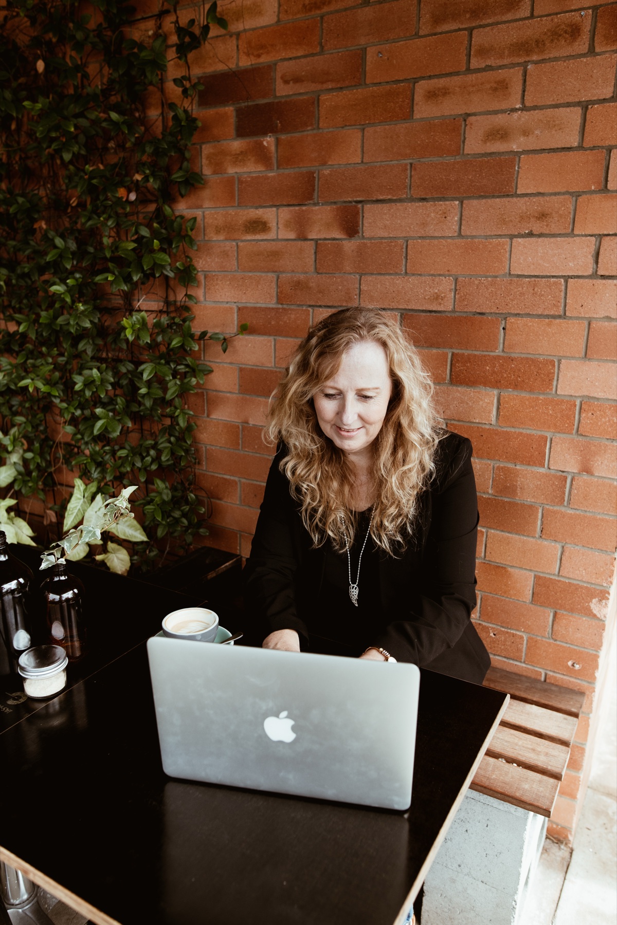 Lyn writing at a table with a laptop and coffee