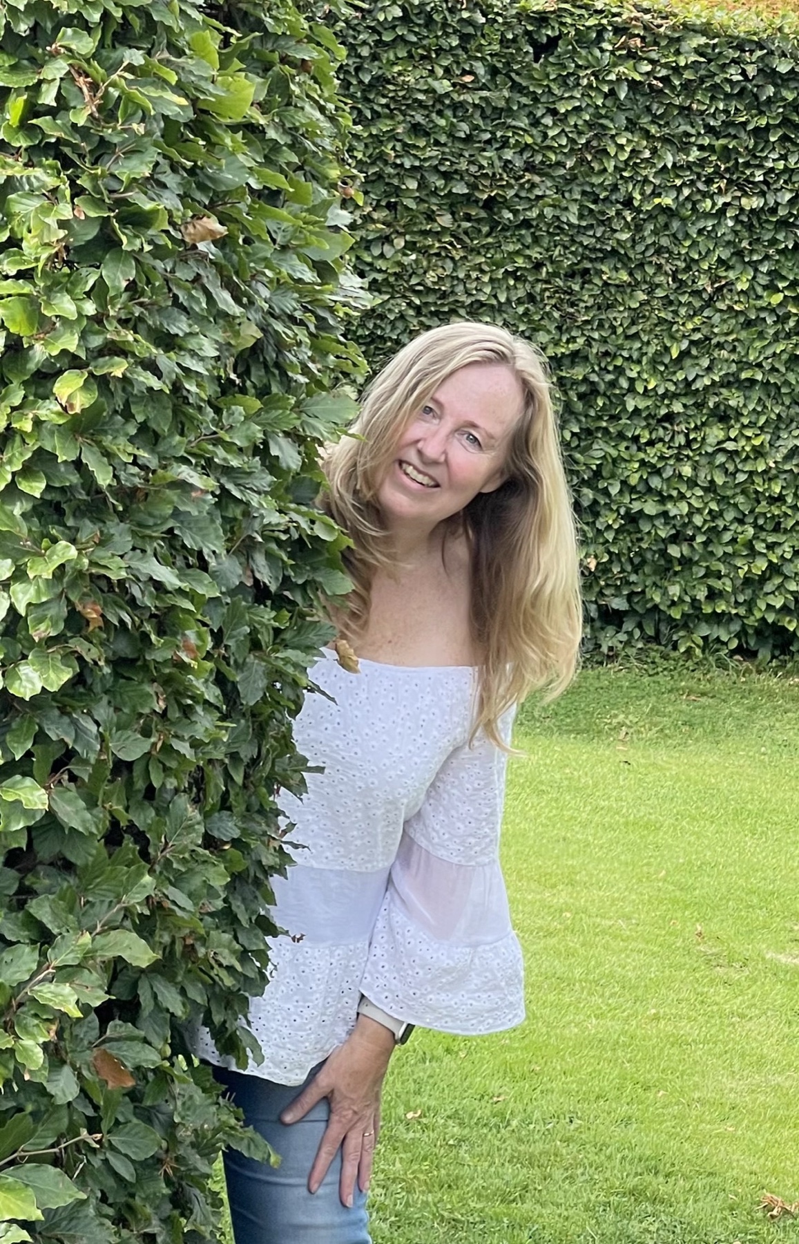 Lyn leaning out from behind a green hedge