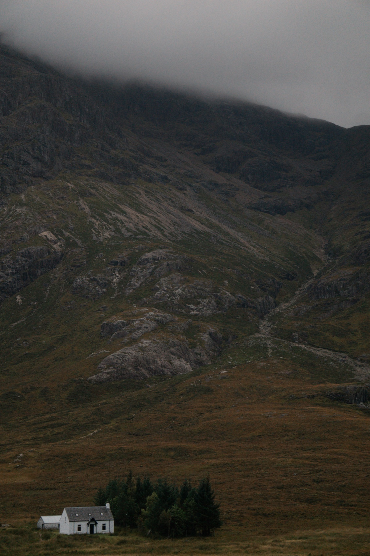 A white cottage in a Scottish glen, mountains rising into cloud