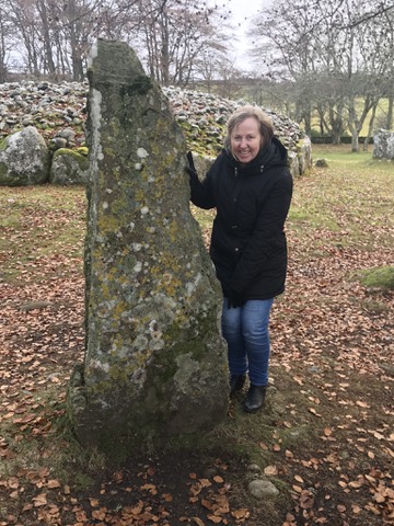 Lyn standing beside an ancient standing stone in Scotland