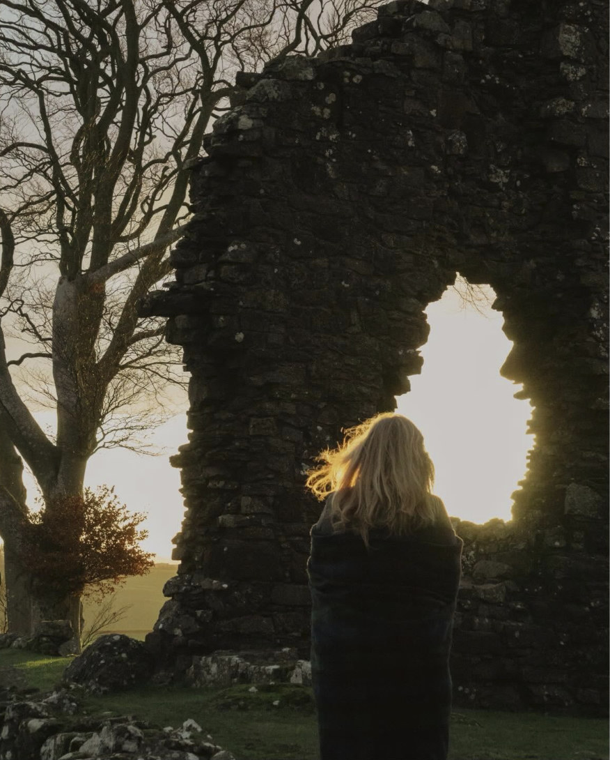 Lyn standing before a sunlit opening in historic Scottish stone ruins.