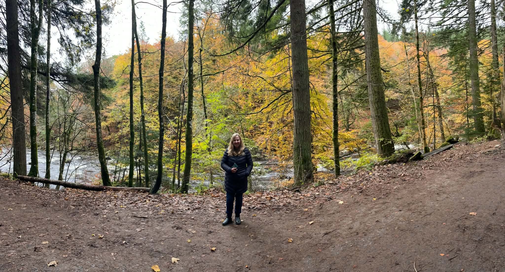Lyn standing among autumn trees beside a river in Scotland